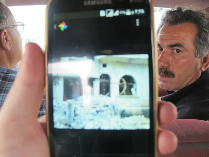A resident of camp shows a photo he had taken of his ruined house in Qamishli, Rojava, caused by the dual war imposed to Kurdish people by both ISIS and Turkey. Thumbnail